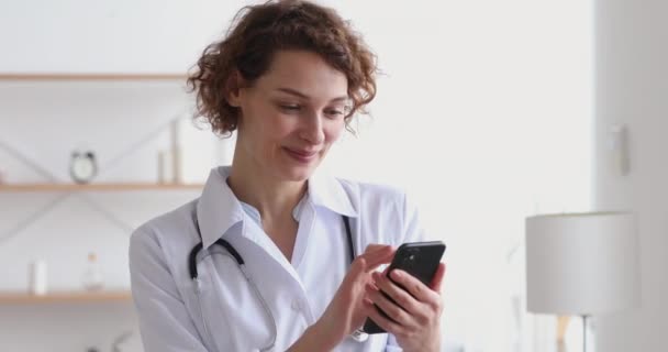 Happy female therapist wearing white coat using smart phone apps — Stock Video