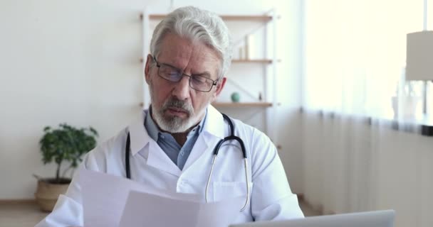 Concentrated serious old doctor reading medical papers analyzing report — Stock Video