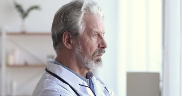 Sérieux réfléchi vieux médecin regardant par la fenêtre penser aux défis — Video