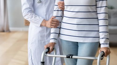 Kadın doktor yaşlı hastaya yürüyüş iskeletinde yardımcı oluyor.