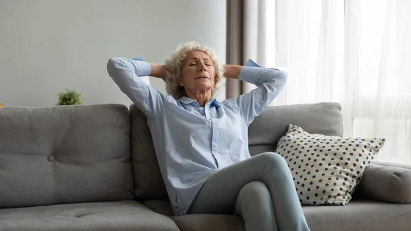 Ältere Frau entspannt sich mit geschlossenen Augen im Wohnzimmer — Stockfoto