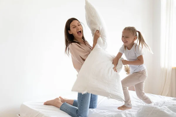 Alegre niña y joven mamá comprometida en la lucha de almohadas —  Fotos de Stock