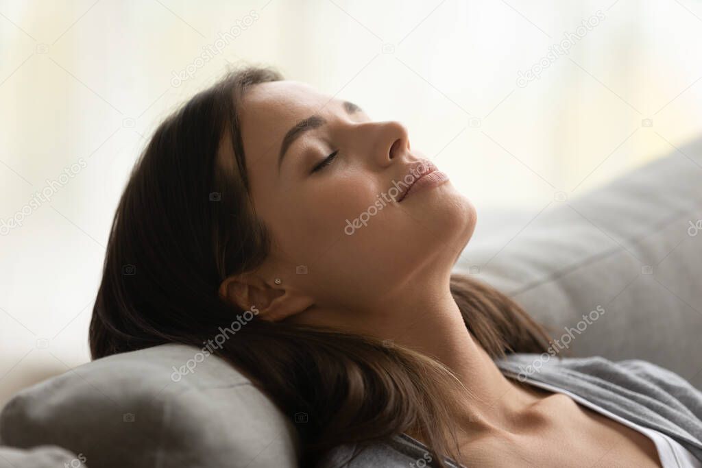 Calm young woman rest on cozy sofa in living room
