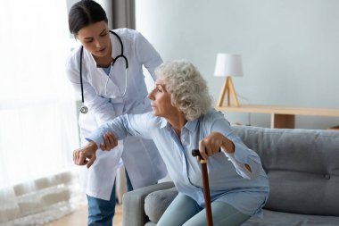 Bayan hemşire yaşlı bayanın ayağa kalkmasına yardım et.