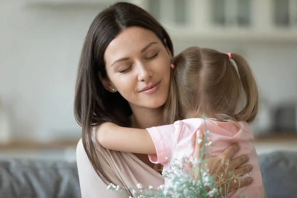 Маленька дочка обіймає молоду маму, представляючи квіти — стокове фото