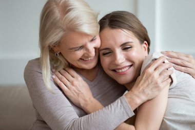 Mutlu gülümseyen anne ve yetişkin kız kucaklaşıp gülüyor.