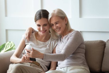 Gülümseyen büyük anne ve yetişkin kız birlikte telefon kullanıyor.