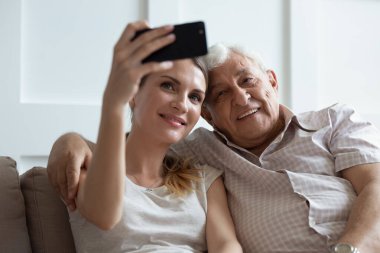 Gülümseyen baba ve yetişkin kız telefonda selfie çekiyor.