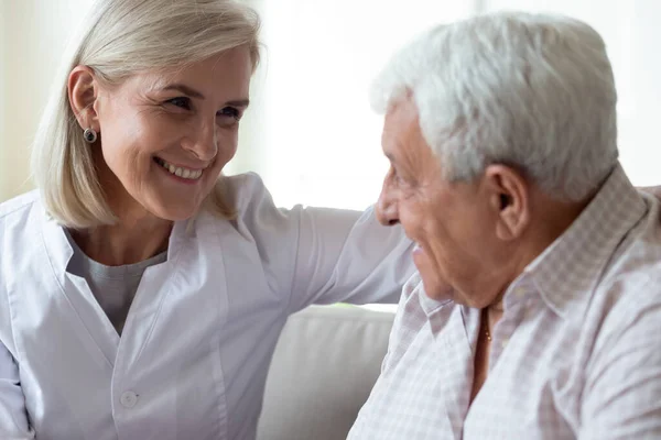 Smilende, middelaldrende kvinnelig lege som snakker med eldre mannlig pasient – stockfoto