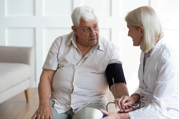 Mature doctor cardiologist checking older man blood pressure during visit — Stock Photo, Image