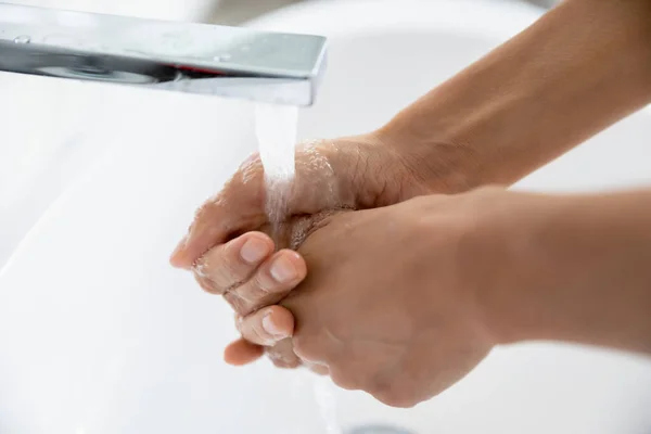 Female wash hands under flowing water close up view