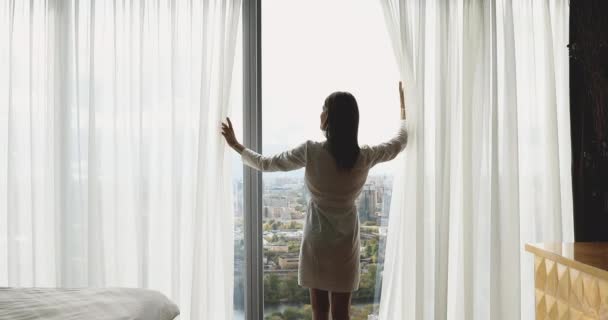 Vista trasera feliz joven morena mujer abriendo cortinas . — Vídeo de stock