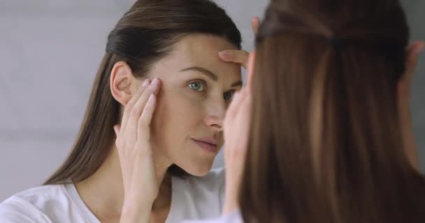 Jonge goed verzorgde dame die haar gezicht aanraakt, kijkend naar spiegel. — Stockvideo