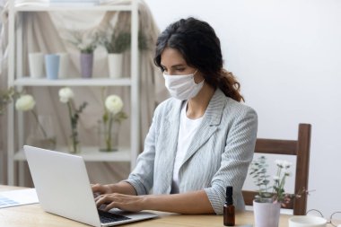 Maskeli kadın ofis laptopunda çalışıyor.