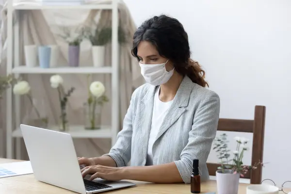 Kvinnliga anställd i medicinsk mask arbete på laptop på kontoret — Stockfoto