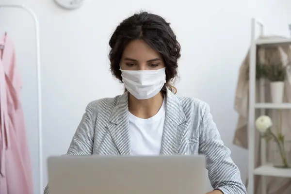 Kvinna i medicinsk mask arbetar på bärbar dator på kontoret — Stockfoto