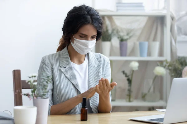 Female employee in mask use hand sanitizer at workplace — Stock Photo, Image