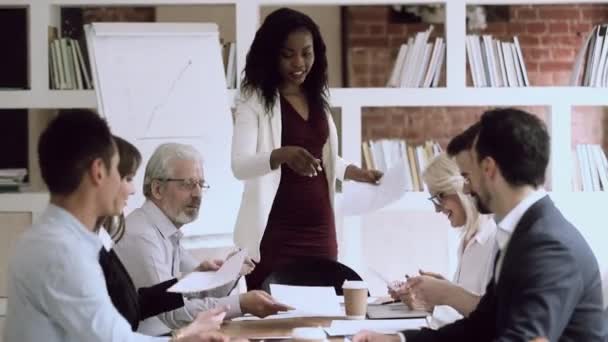 Black female boss give papers to employees group at meeting — Stock video