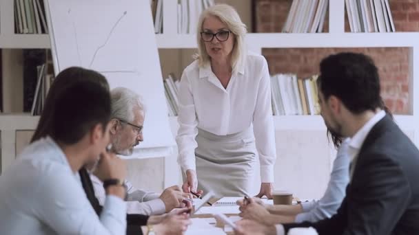 Oude vrouwelijke baas aan het praten op groepsvergadering wijzend op papierwerk — Stockvideo