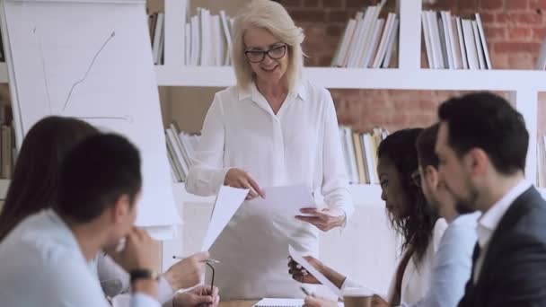 Older female boss presenting work plan give papers to employees — Stock Video