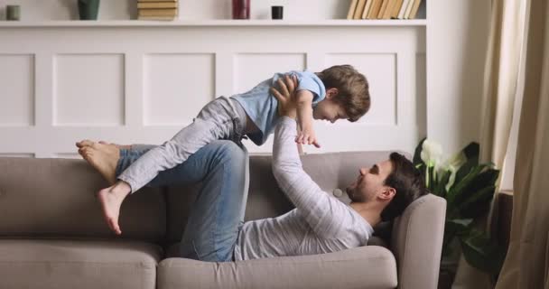 Forte jovem pai levantando nos braços pequeno filho brincalhão — Vídeo de Stock