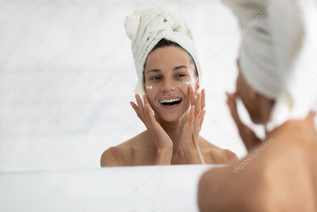 Woman looking in mirror while applied facial cream