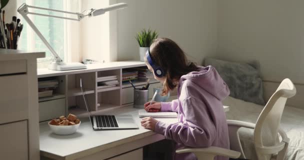 Chica adolescente con auriculares que estudian en línea usando el ordenador portátil haciendo notas — Vídeo de stock