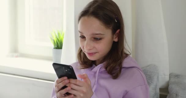 Χαμογελώντας έφηβος κορίτσι χρησιμοποιώντας smartphone κουβέντα με τους φίλους στο σπίτι — Αρχείο Βίντεο