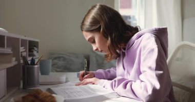Genç kız ders çalışıyor, ders kitabı okuyor, çalışma masasında notlar alıyor.