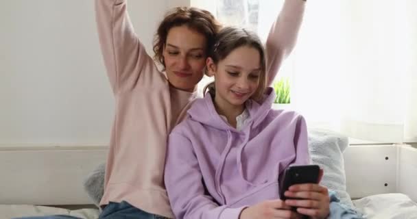 Щаслива дочка-підліток, що показує мамі смішне музичне відео на смартфон — стокове відео