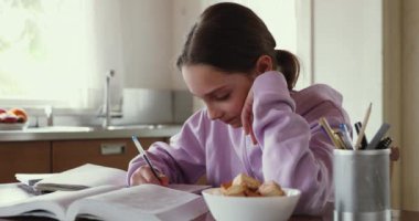 Evde mutfak masasında okuyan odaklanmış genç kız öğrenci.