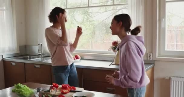 Счастливые дочь-подросток и мама с удовольствием поют и готовят — стоковое видео
