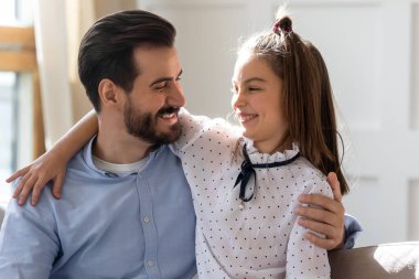 Gülümseyen genç baba küçük kızı kucaklıyor, evde şakalaşıyor..