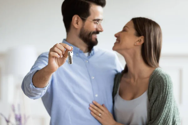 Focus on smiling man cuddling wife, showing keys to camera. — Stock Photo, Image