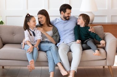 Sevecen genç ebeveynler kanepede dinleniyor, küçük çocuklara sarılıyorlar..