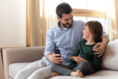 Mutlu baba küçük çocuğa sarılıyor, komik mobil uygulamalar gösteriyor..