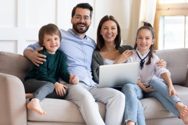 Mutlu ve çocuklu bir aile bilgisayarla kanepede dinleniyor..