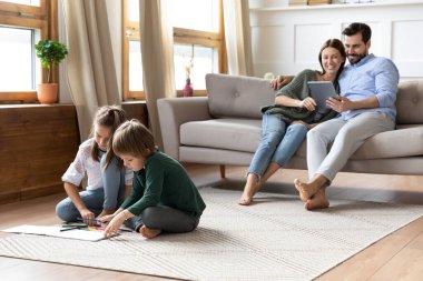 Oyuncak çocuklar resim çizerken ebeveynler dijital tablet kullanıyor.