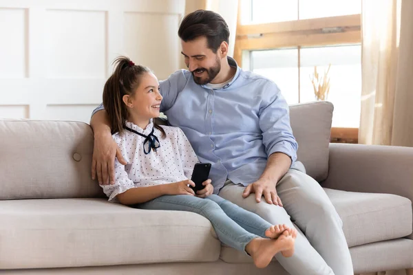 Sonriente papá abrazo bastante linda hija, utilizando el teléfono móvil . —  Fotos de Stock