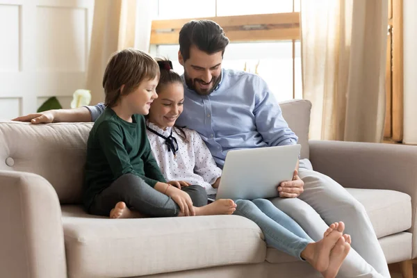Gülümseyen genç baba çocuklarla bilgisayarda film izliyor..