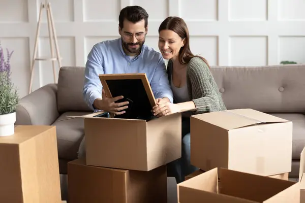 Feliz joven familia pareja desempacar pertenencias, mirando la foto de la familia . — Foto de Stock