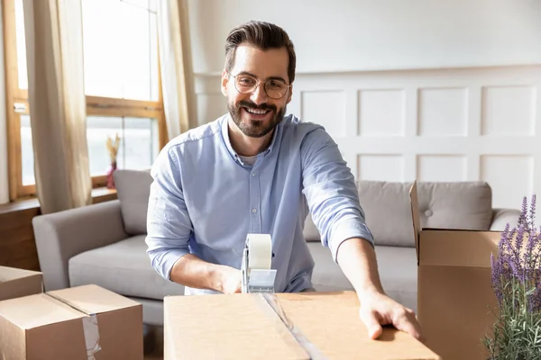 Smiling young bearded man packing personal belongings in cardboard boxes. — Stock Photo, Image