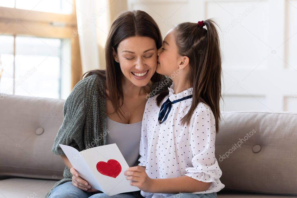 Adorable little girl kissing mommy, presenting handmade card.