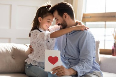 Minnettar genç baba el yapımı tebrik kartı tutuyor, kızını kucaklıyor..