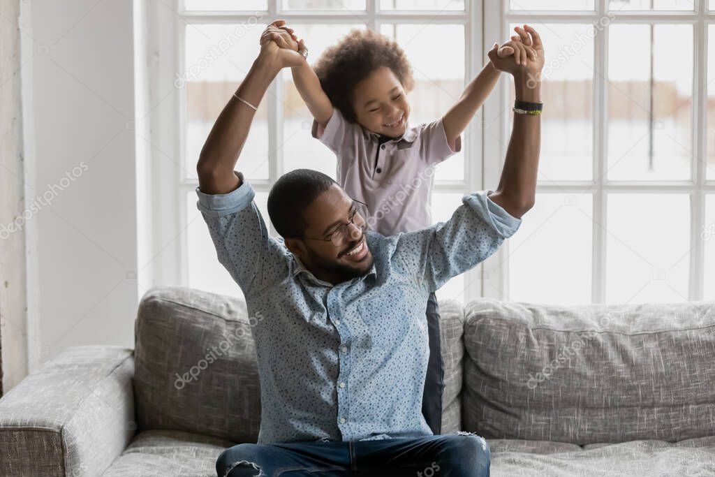 African loving father sitting on couch playing with little son