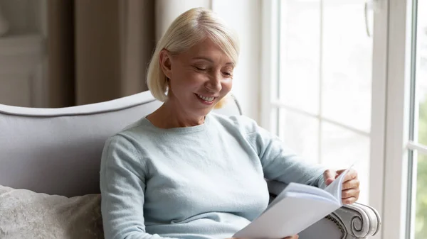 Glückliche ältere Frau liest Buch entspannt zu Hause — Stockfoto