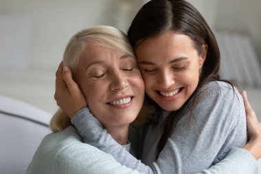 Sevgi dolu yaşlı bir anne ve yetişkin bir kız evde sarılıyor.
