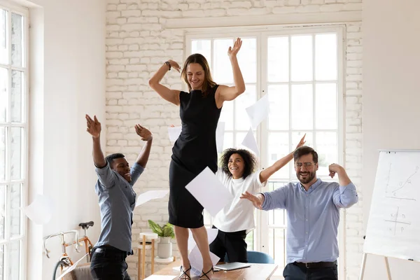 Diversos empleados corporativos bailando en la sala de juntas lanzan papeles celebrando el éxito — Foto de Stock