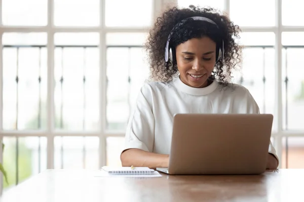 African businesswoman wearing headphones using laptop at work typing message — Stock Photo, Image