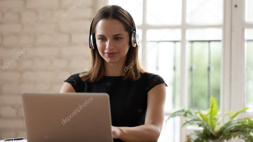 Attractive woman wearing headphones sitting at desk typing on laptop
